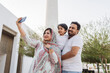 © Daniel Gonzalez/Stocksy - Cheerful Indian family taking selfie on smartphone on street