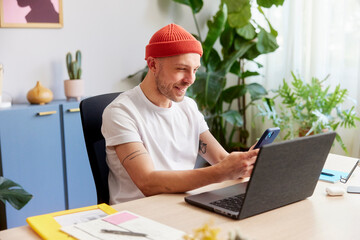 Delighted man with laptop chatting on smartphone