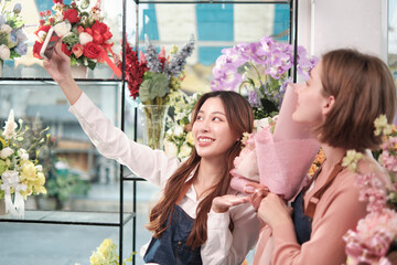 E-commerce business partner, two young female florist workers show floral arrangement, online live streaming, and selfies with smartphone application in bright flower shop, beautiful blossoms store.