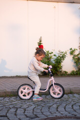 Wall Mural - A little girl in a pink suit rides a pink runner in the rays of the sunset.