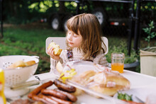 Little Girl Sitting At Dinner Table On Porch During Bbq