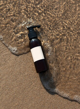 The Cosmetic Product Bottle On The Sand Covering With Sea Wave.