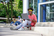 © Jovo Jovanovic/Stocksy - Student using laptop and headphones on college steps.