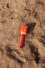 Children's Red Toy Sad Toy Shovel Lying On A Sand Of Beach 