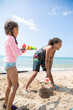 © Anya Brewley Schultheiss/Stocksy - Child spraying her sister with a water gun while at the beach