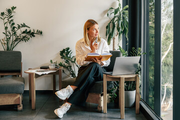 Wall Mural - Mature business woman working on laptop, making notes in cozy coworkign space interior