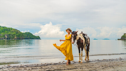 Traveler woman wearing yellow dress on vacation beach with horse joy nature scenic landscape, Leisure tourist travel Satun Phuket Thailand summer holiday trip, Tourism beautiful destination place Asia