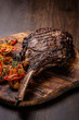 A large fried piece of meat on the bone Tomahawk lies on a wooden board with grilled vegetables