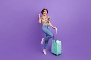 Wall Mural - Full length portrait of delighted overjoyed person hold suitcase raise fist achievement luck isolated on purple color background