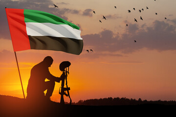 Silhouette of soldier kneeling with his head bowed against the sunrise or sunset and UAE flag. Commemoration Day.