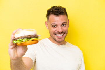 Wall Mural - Young caucasian man holding a burger isolated on yellow background