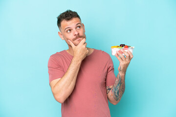 Wall Mural - Young caucasian man holding a bowl of fruit isolated on blue background having doubts