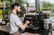 © LIGHTFIELD STUDIOS - side view of bearded barista in apron working with coffee machine in coffee shop