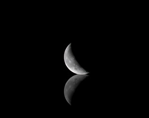 Wall Mural - waning crescent moon with reflection on black background 7-11-2023