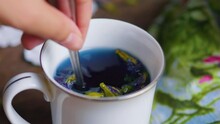 Female Hand Stirring Blue Thai Anchan Butterfly Pea Flower Tea In Mug.