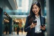 © sirisakboakaew - Busy young professional Asian businesswoman holding mobile phone walking on a big city street.