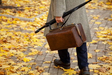 Man with carpetbag and coat walks along autumn alley....