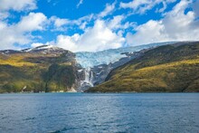 Waterfall Cascading Down From A Mountain Range Into The Tranquil Beagle Channel In Chilean Fjords