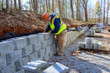 © ungvar - Cement blocks are being used by construction worker to build retaining wall during development of new property.