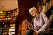 © Marko Geber - Young smiling caucasian woman with short hair using a smart phone in a library