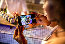 Young African Woman Taking A Photo With Her Smart Phone Of The Sushi A Chef Prepared In A Sushi Bar