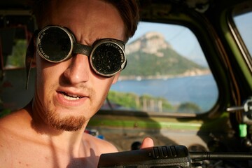 Sticker - Caucasian man wearing sunglasses and no shirt sitting in a boat holding a radio receiver in Sardinia