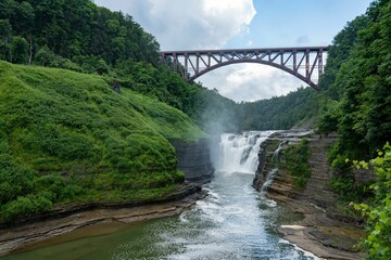 Scenic view of a bridge crossing a waterfall with a lush green forest in Letchworth State Park