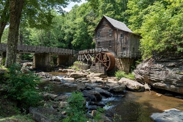 Wall Mural - Wooden house with a cascading stream running through a lush green forest in Babcock State Park