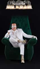 Wall Mural - rich man in a white suit sits in a chair, black studio background