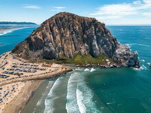 Aerial View Of Morro Rock With Multiple Cars Parked Along The Sandy Shoreline. California, USA.