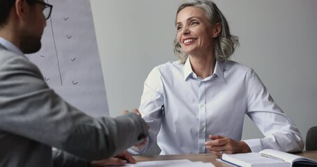 Canvas Print - Positive confident mature executive, employer woman hiring candidate after successful job interview, giving handshake to younger business professional man, hoping for collaboration, partnership