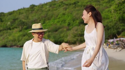 Wall Mural - Happy Asian family couple holding hands walking together on seaside at tropical island beach at sunset. Husband and wife enjoy and fun outdoor lifestyle travel nature ocean on summer holiday vacation