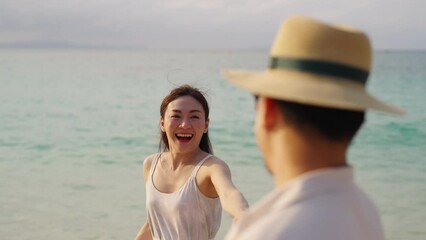 Wall Mural - Happy Asian family couple holding hands walking together on seaside at tropical island beach at sunset. Husband and wife enjoy and fun outdoor lifestyle travel nature ocean on summer holiday vacation