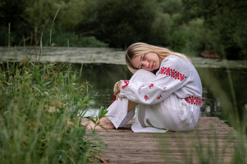 Portrait of a beautiful fair-haired girl in national clothes near a forest river.