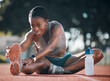 Sports, stretching and exercise with a woman outdoor on a track for running, training or workout. Happy African athlete person at stadium for legs stretch, fitness and muscle warm up or body wellness