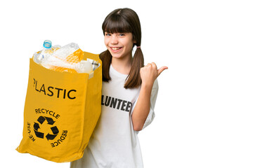 Wall Mural - Little caucasian girl holding a bag full of plastic bottles to recycle over isolated background pointing to the side to present a product