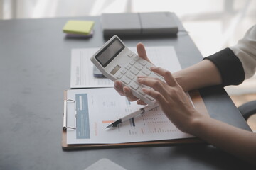 Asian Businesswoman Using laptop computer and working at office with calculator document on desk, doing planning analyzing the financial report, business plan investment, finance analysis concept.