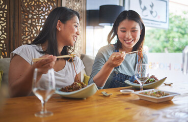 Wall Mural - Restaurant, girl friends and lunch with food, noodles and cafe happy from bonding. Asian women, eating and plate together with friendship smile at a table hungry with chopsticks at Japanese bar