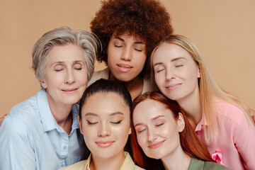 Wall Mural - Group of multiethnic women with eyes closed wearing breast cancer pink ribbon isolated on beige background. Health care, prevention. Breast cancer awareness month