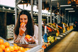 © dvulikaia - Young beautiful dark-haired woman picks oranges at  local farmer's market.