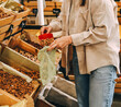 © dvulikaia - Close-up of  young woman pouring almonds into  mesh reusable bag at market.