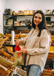 © dvulikaia - Young woman pouring almonds into  mesh reusable bag at market.
