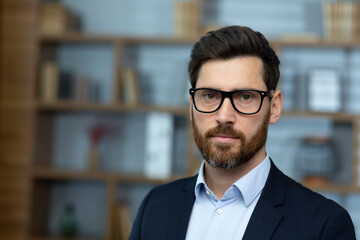 Wall Mural - Close up of mature experienced lawyer, serious man in glasses and business suit inside classic office, businessman looking at camera thinking.