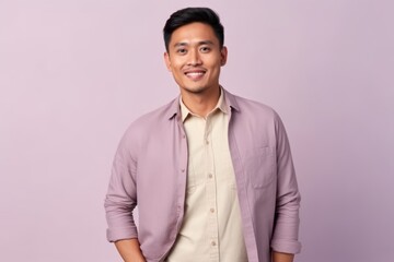 Wall Mural - Portrait of a happy young asian man standing against purple background