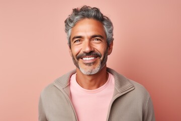 Portrait of a handsome mature Indian man smiling at the camera while standing against a pink background