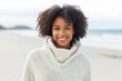 © Leon Waltz - Lifestyle portrait of a Nigerian woman in her 20s in a beach background wearing a cozy sweater