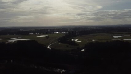 Wall Mural - Aerial view of vast green fields and trees by a pond with gray cloudy sky on the horizon