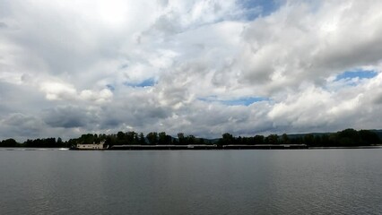 Wall Mural - Timelapse footage of white clouds in blue sky over windy pond water with trees