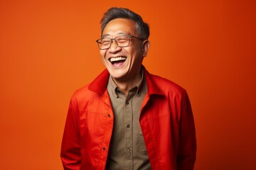 Wall Mural - Portrait of a happy asian man in red jacket and glasses on orange background