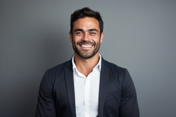 Portrait of a smiling young businessman looking at camera while standing against grey background